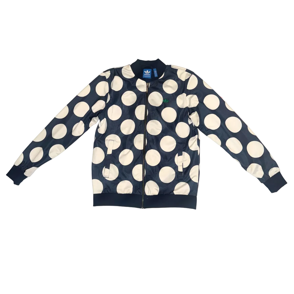 A navy blue bomber jacket with a large white polka dot pattern, laid flat on a light-colored surface. The jacket features a full front zipper, ribbed collar, cuffs, and hem, and an Adidas logo is visible on the inner neck label.