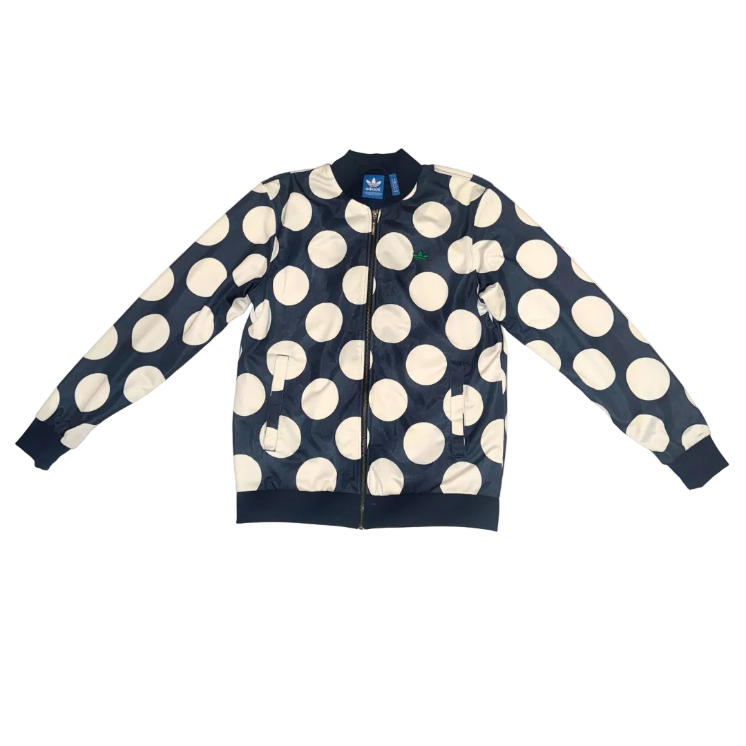 A navy blue bomber jacket with a large white polka dot pattern, laid flat on a light-colored surface. The jacket features a full front zipper, ribbed collar, cuffs, and hem, and an Adidas logo is visible on the inner neck label.