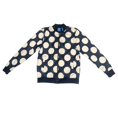 A navy blue bomber jacket with a large white polka dot pattern, laid flat on a light-colored surface. The jacket features a full front zipper, ribbed collar, cuffs, and hem, and an Adidas logo is visible on the inner neck label.