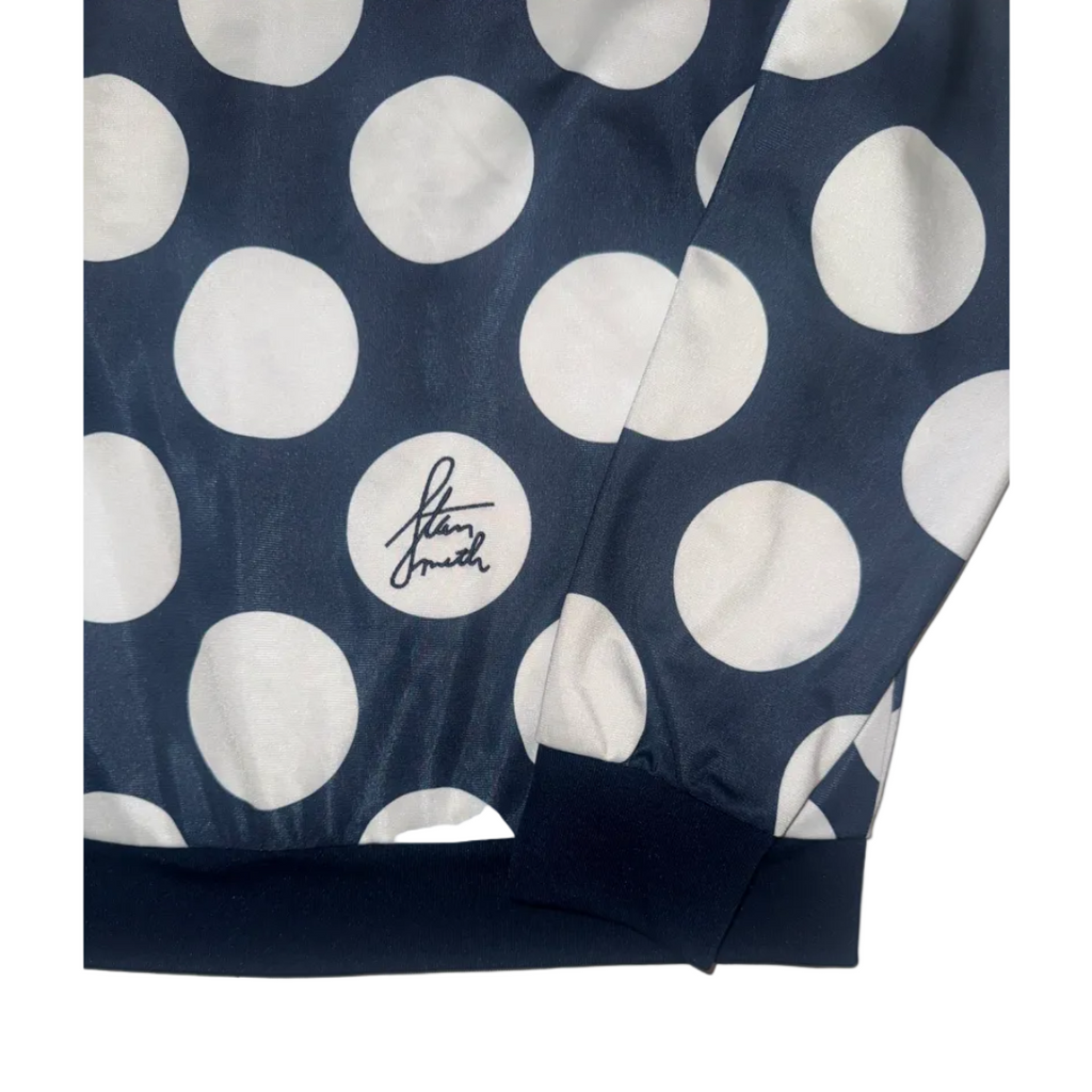 A navy blue jacket or windbreaker featuring a bold white polka dot pattern, with a white circular patch on the chest displaying the signature 'Stan Smith'.