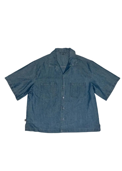 A short-sleeve button-up shirt in blue denim, featuring a pointed collar, button front, and two chest pockets, laid flat against a white background.