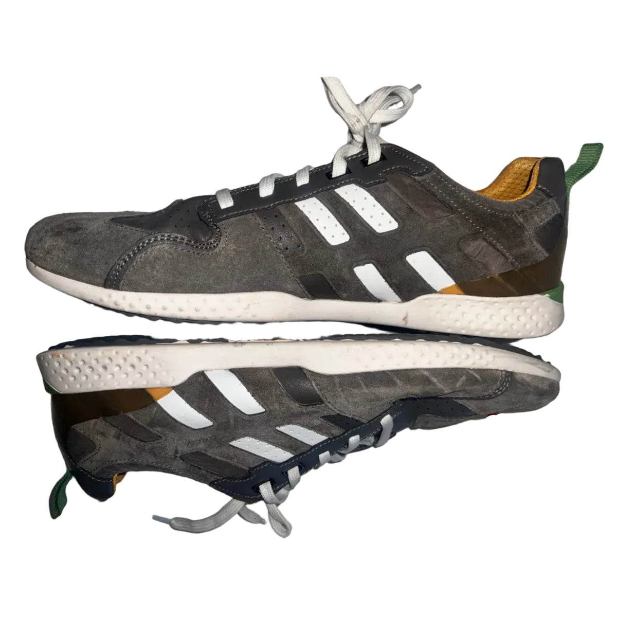 A pair of Geox low-top sneakers shown from the side and sole views, featuring a dark gray suede and synthetic upper with white three-stripes, a white midsole, and small orange and green accents.