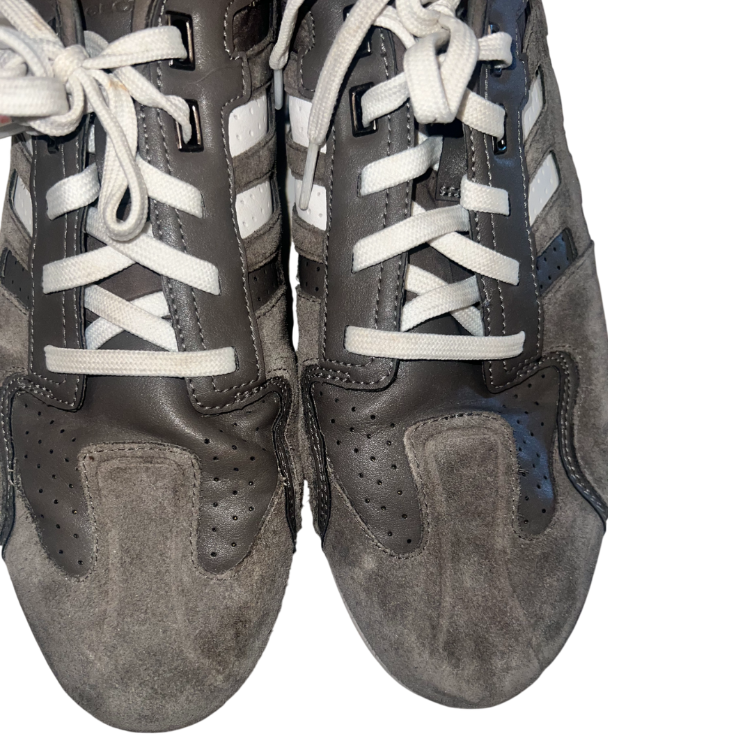 A pair of low-top sneakers in dark gray suede and leather with white laces and white side stripes, shown against a plain white background.