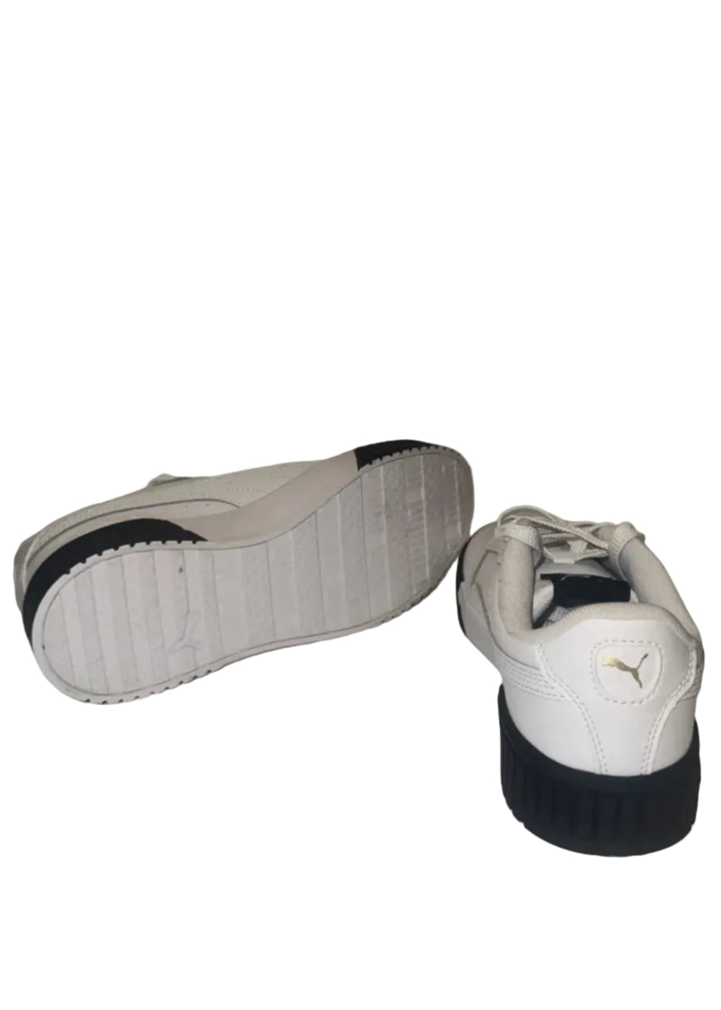 A pair of white Puma sneakers with black soles, with one shoe showing its sole and the other showing the back heel with the Puma logo.