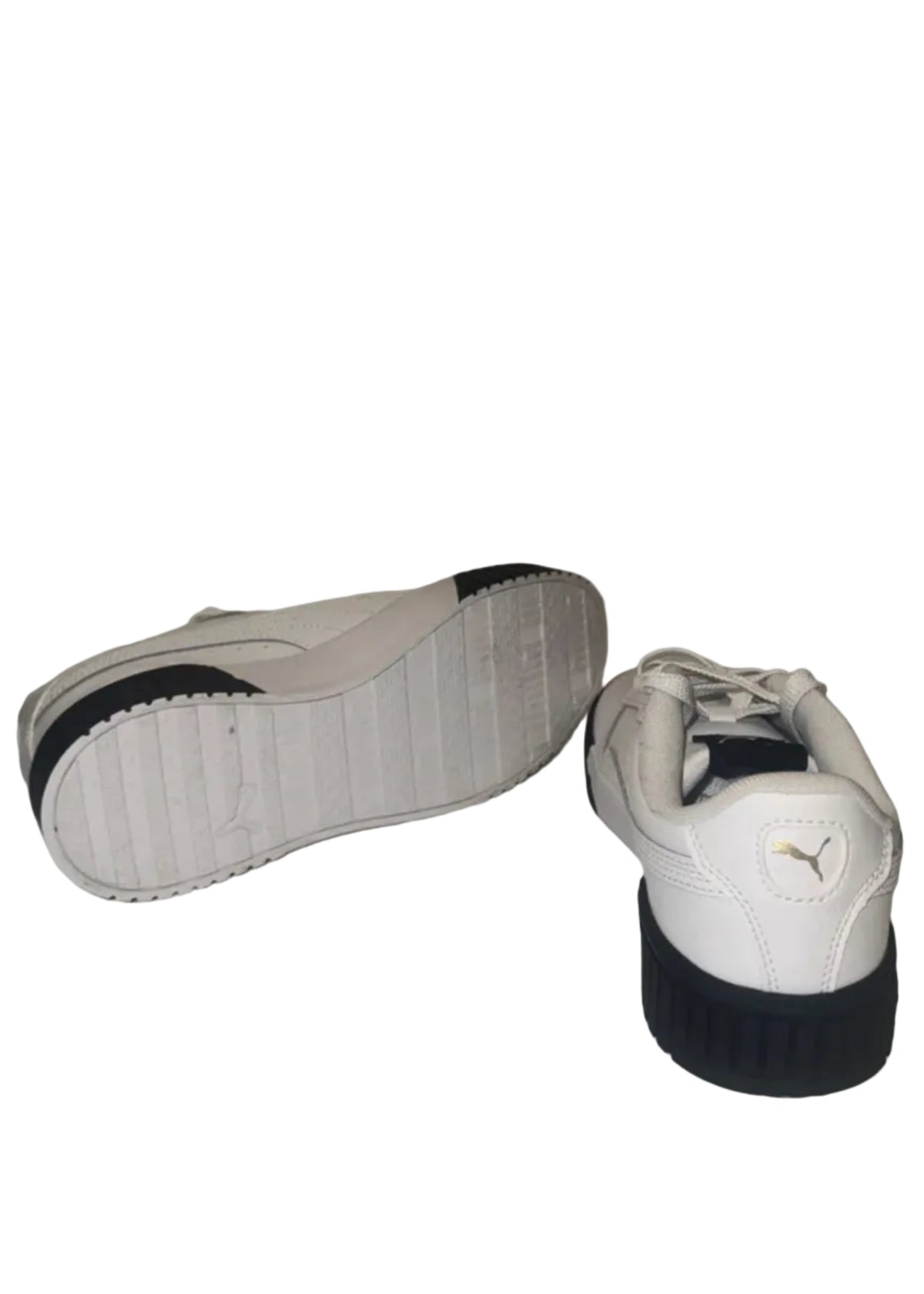A pair of white Puma sneakers with black soles, with one shoe showing its sole and the other showing the back heel with the Puma logo.
