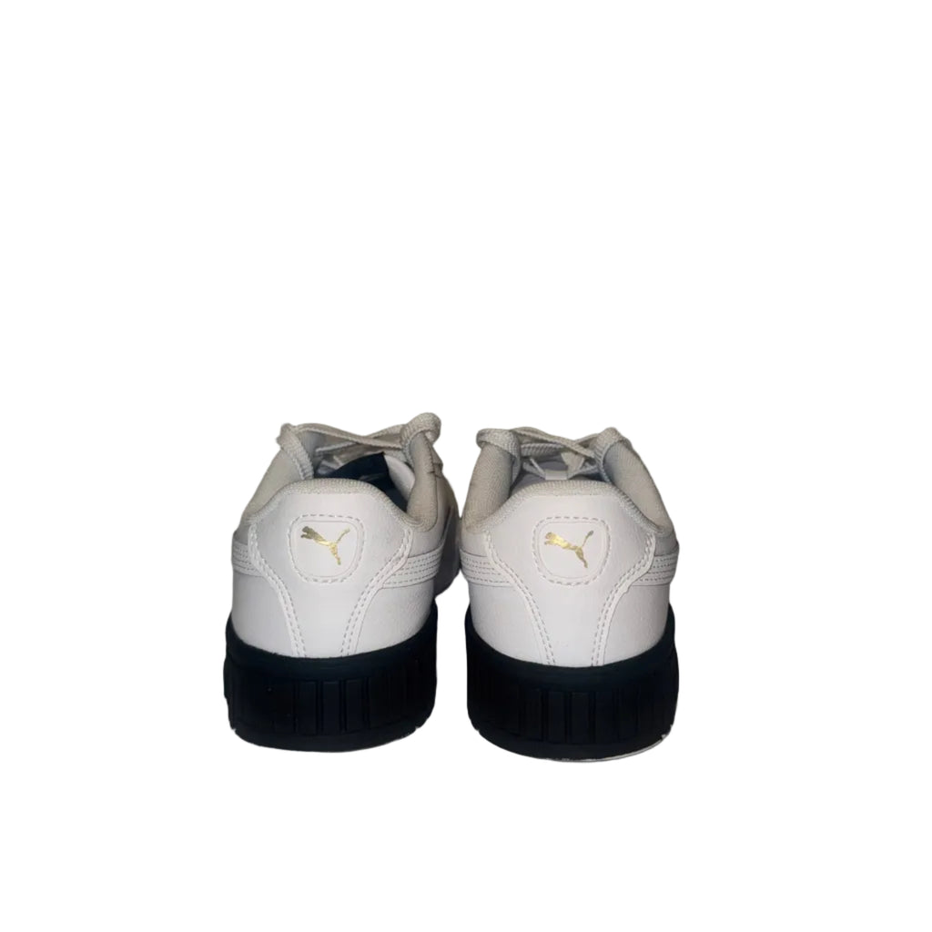 A pair of white Puma sneakers viewed from the back, featuring a white leather upper, a small gold Puma cat logo on the heel, and a thick black sole.